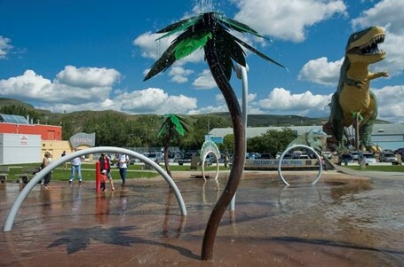 a water park with water spraying features with the worlds largest dinosaur statue in the background